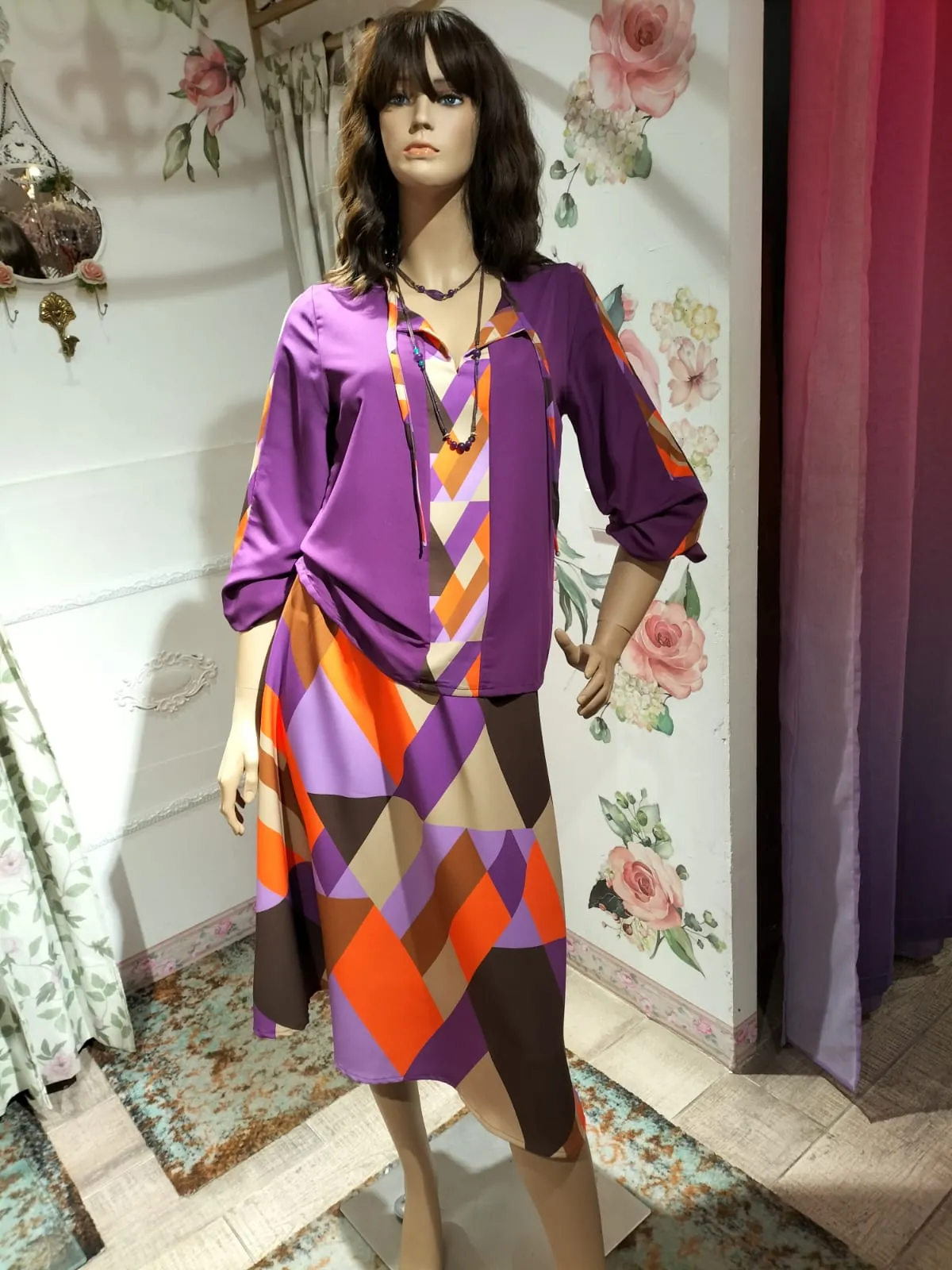 Maniquí luciendo blusa y falda estampada en tonos morados y naranjas