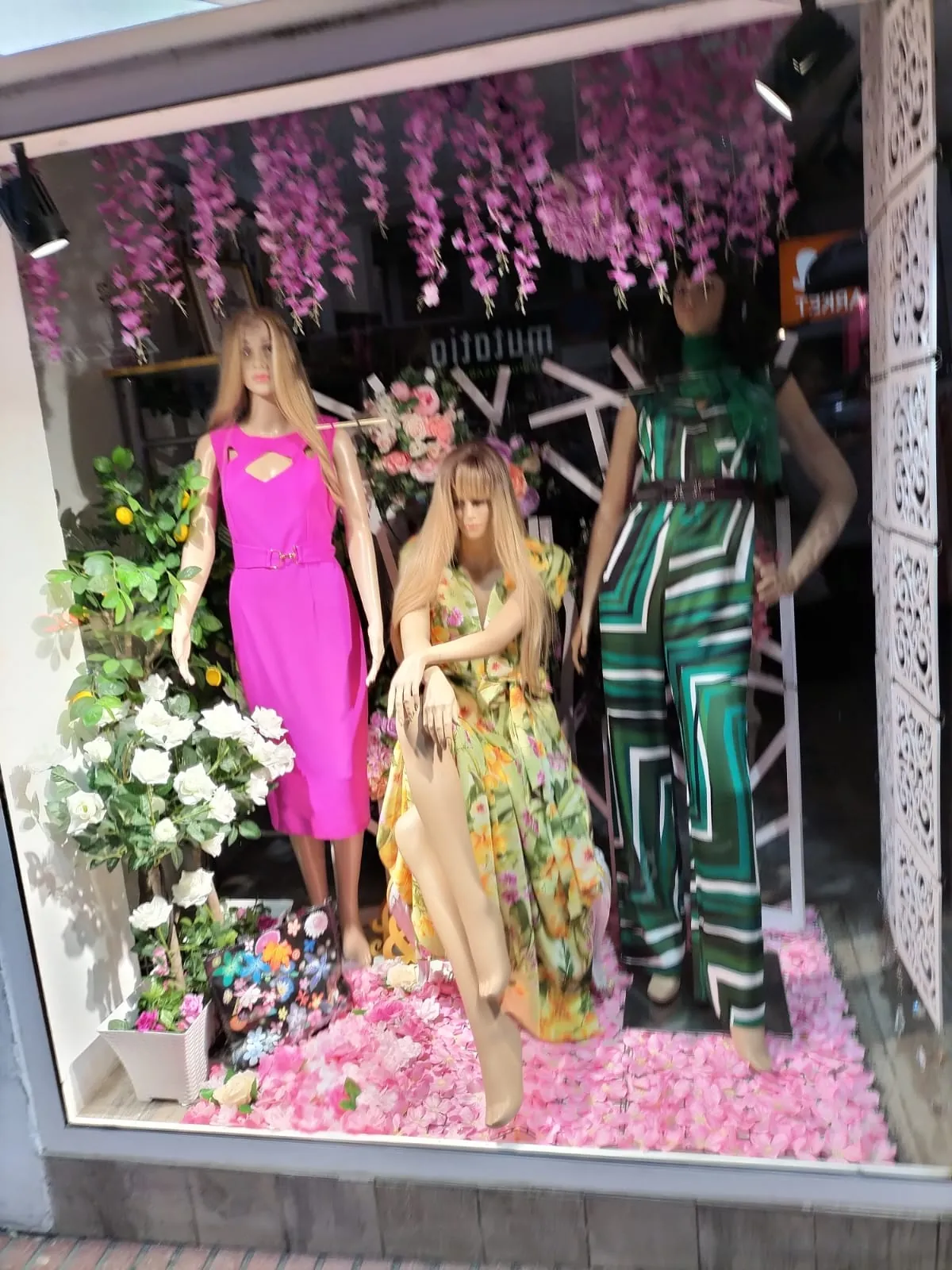 Escaparate con maniquís vestidos de fiesta en rosa, estampado floral y verde